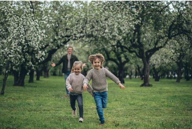 Imagen de hermanos niños corriendo por un campo con su madre persiguiéndoles.